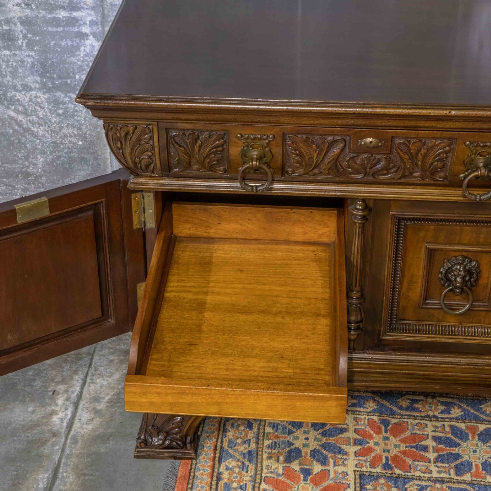 A low carved dark walnut sideboard featuring four panelled doors with cast brass lion mask drop handles below a carved relief frieze. View III