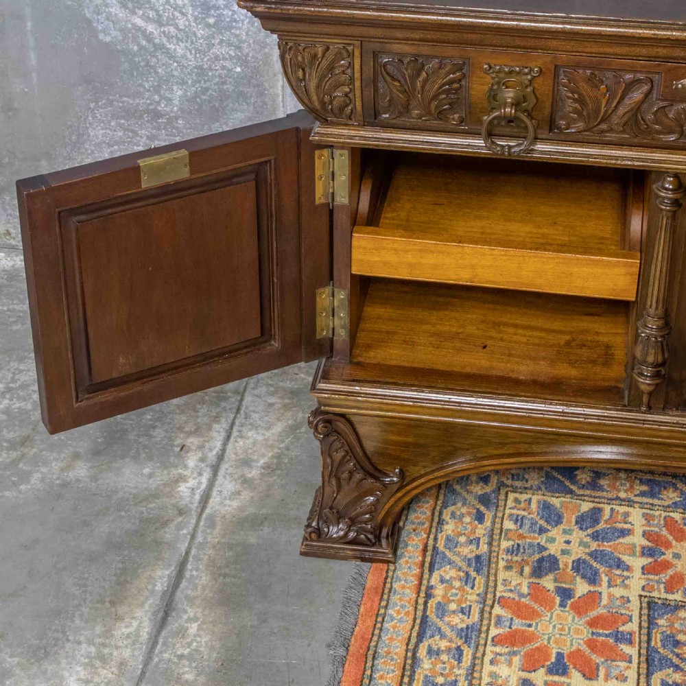 A low carved dark walnut sideboard featuring four panelled doors with cast brass lion mask drop handles below a carved relief frieze. View IV