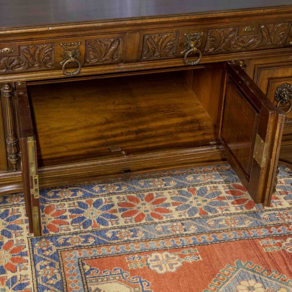 A low carved dark walnut sideboard featuring four panelled doors with cast brass lion mask drop handles below a carved relief frieze. View VI