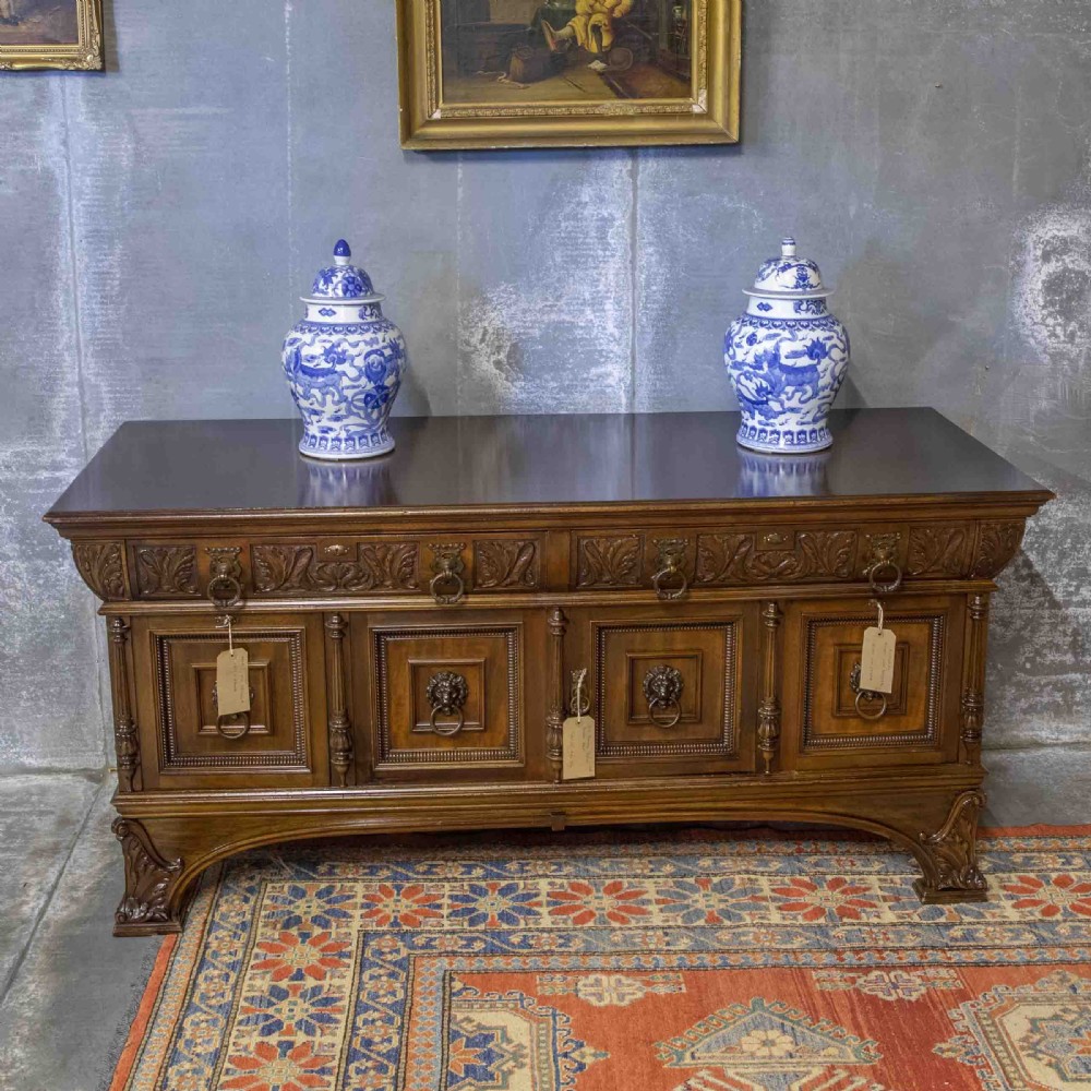 A low carved dark walnut sideboard featuring four panelled doors with cast brass lion mask drop handles below a carved relief frieze. View VII