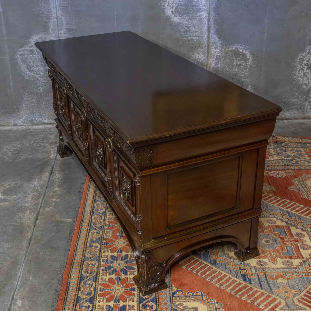 A low carved dark walnut sideboard featuring four panelled doors with cast brass lion mask drop handles below a carved relief frieze. View IX