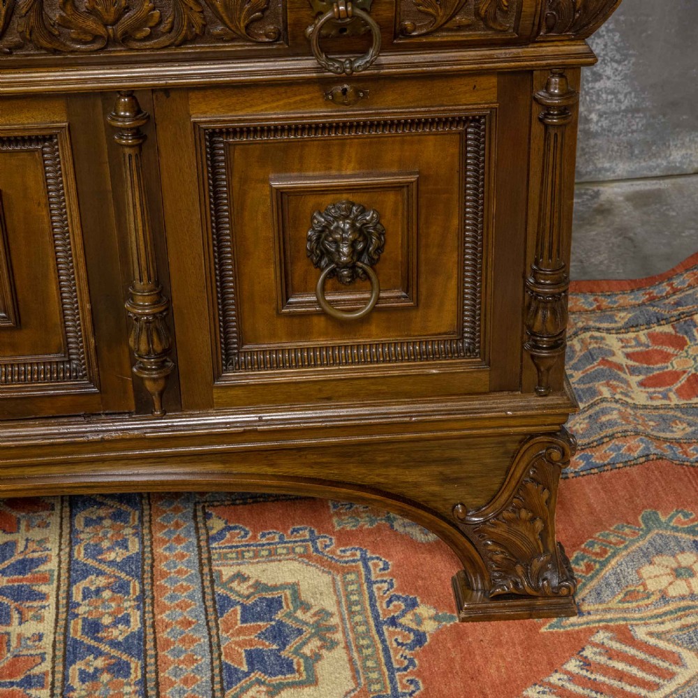 A low carved dark walnut sideboard featuring four panelled doors with cast brass lion mask drop handles below a carved relief frieze. View X