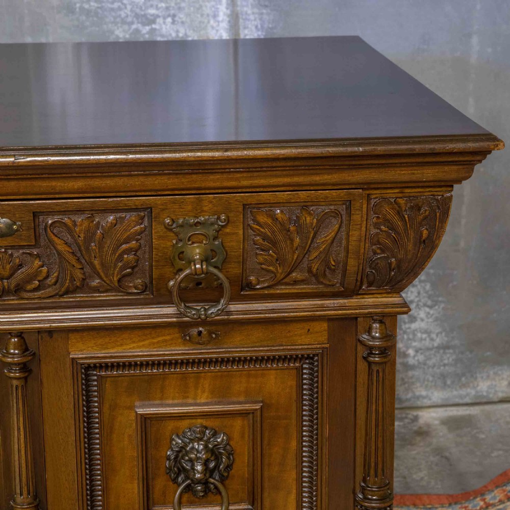 A low carved dark walnut sideboard featuring four panelled doors with cast brass lion mask drop handles below a carved relief frieze. View XI