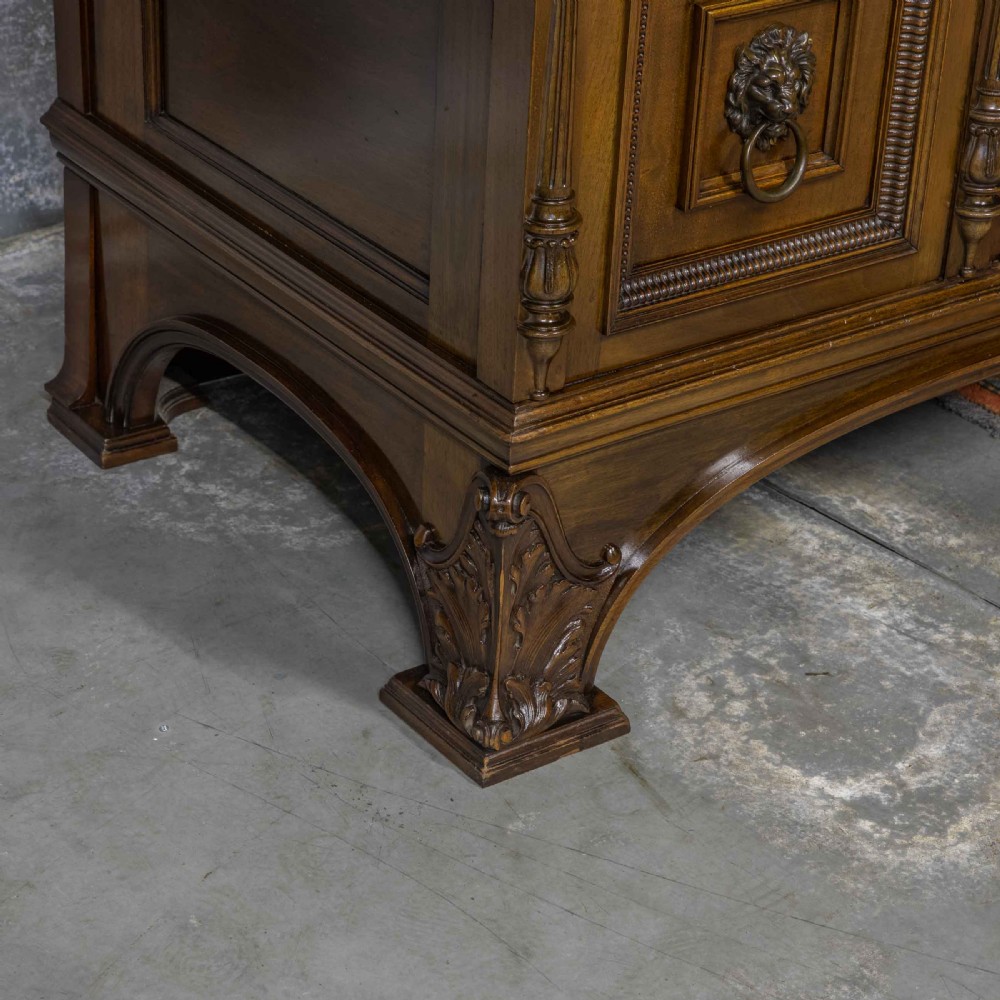 A low carved dark walnut sideboard featuring four panelled doors with cast brass lion mask drop handles below a carved relief frieze. View XII