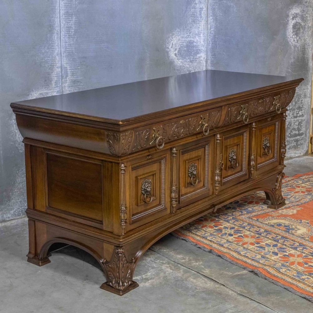 A low carved dark walnut sideboard featuring four panelled doors with cast brass lion mask drop handles below a carved relief frieze. View XIII