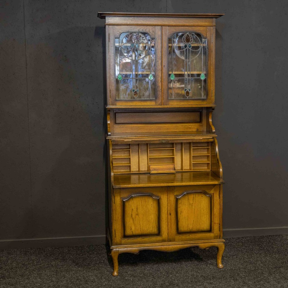 An Edwardian oak roll top bureau bookcase featuring an upper cabinet with two leaded glass doors, a central curved tambour writing section, and a two-door lower cupboard. View II