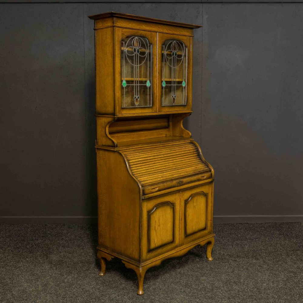 An Edwardian oak roll top bureau bookcase featuring an upper cabinet with two leaded glass doors, a central curved tambour writing section, and a two-door lower cupboard. View III