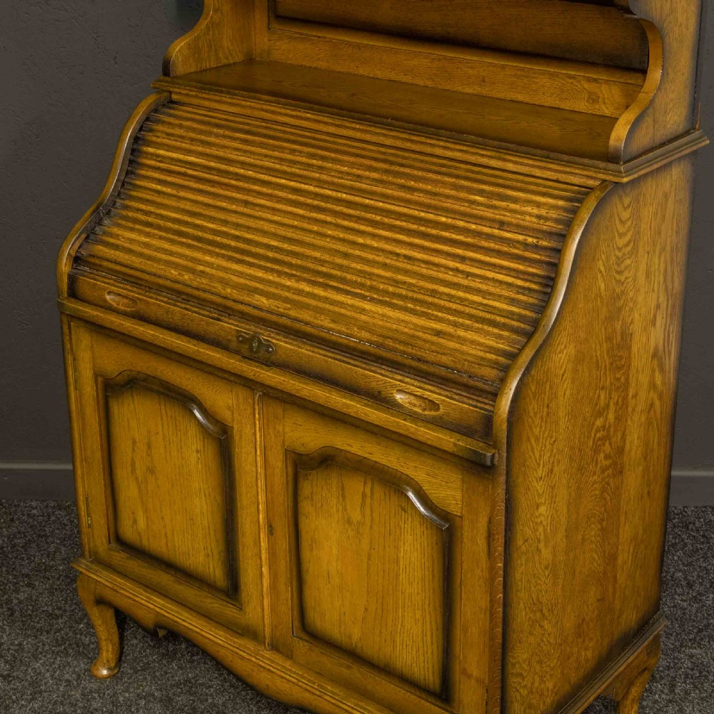 An Edwardian oak roll top bureau bookcase featuring an upper cabinet with two leaded glass doors, a central curved tambour writing section, and a two-door lower cupboard. View IV