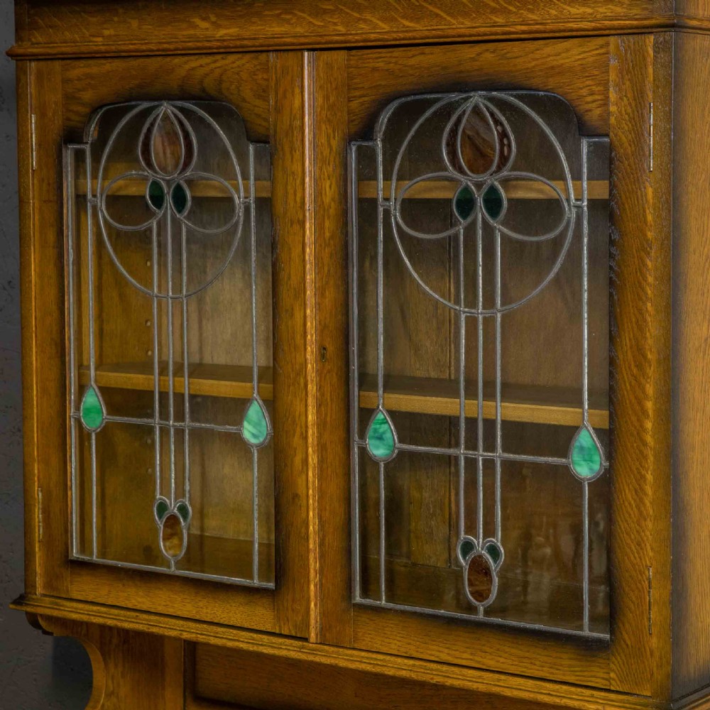 An Edwardian oak roll top bureau bookcase featuring an upper cabinet with two leaded glass doors, a central curved tambour writing section, and a two-door lower cupboard. View V