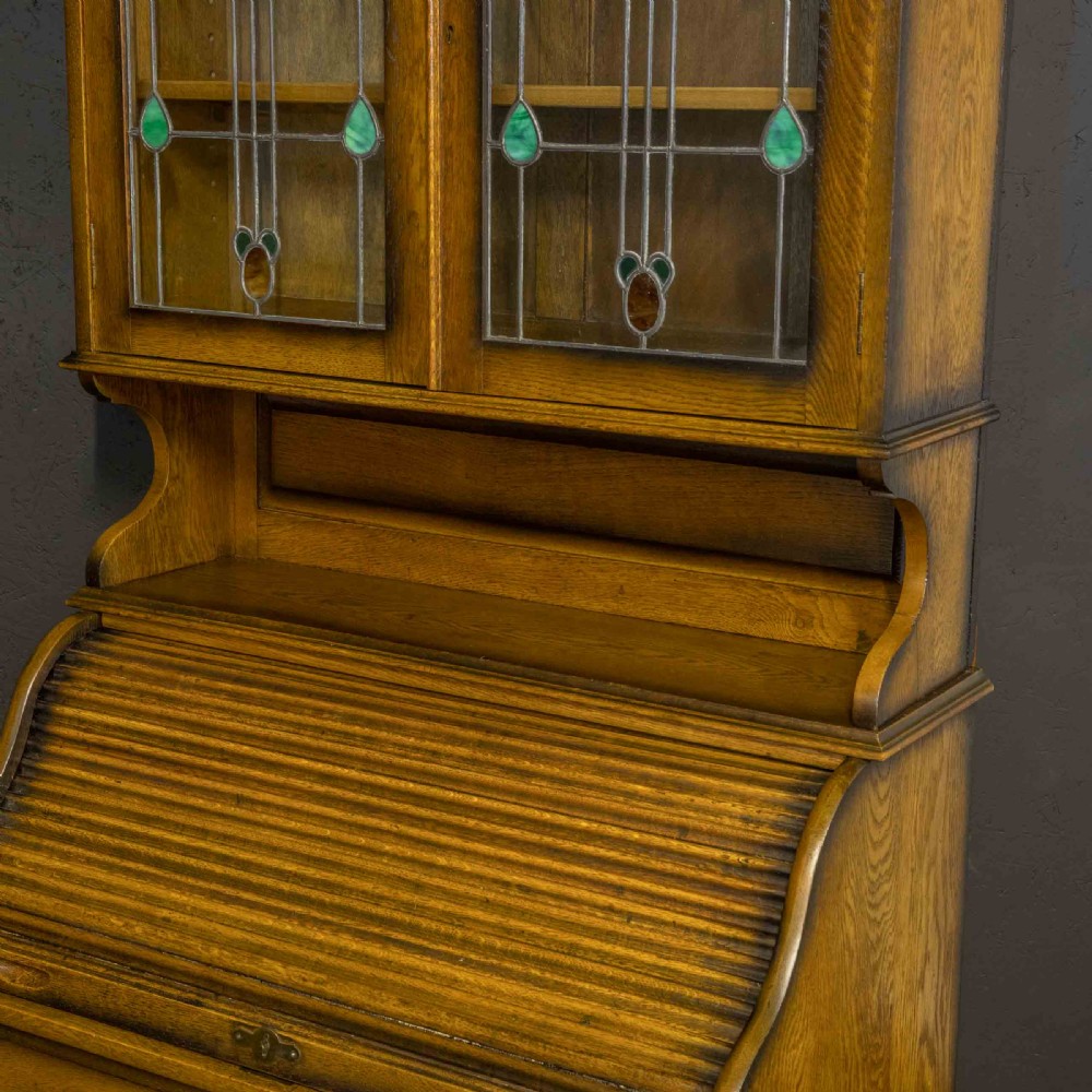 An Edwardian oak roll top bureau bookcase featuring an upper cabinet with two leaded glass doors, a central curved tambour writing section, and a two-door lower cupboard. View VI