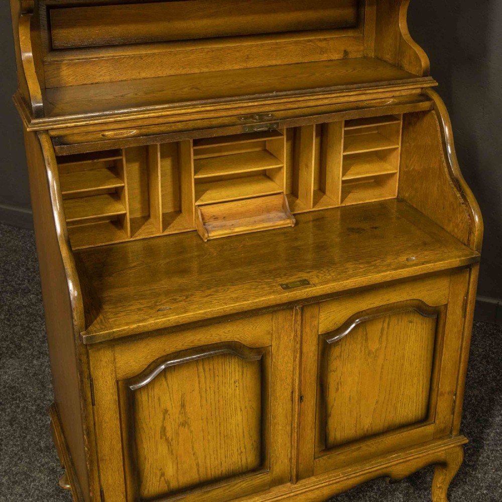 An Edwardian oak roll top bureau bookcase featuring an upper cabinet with two leaded glass doors, a central curved tambour writing section, and a two-door lower cupboard. View VII