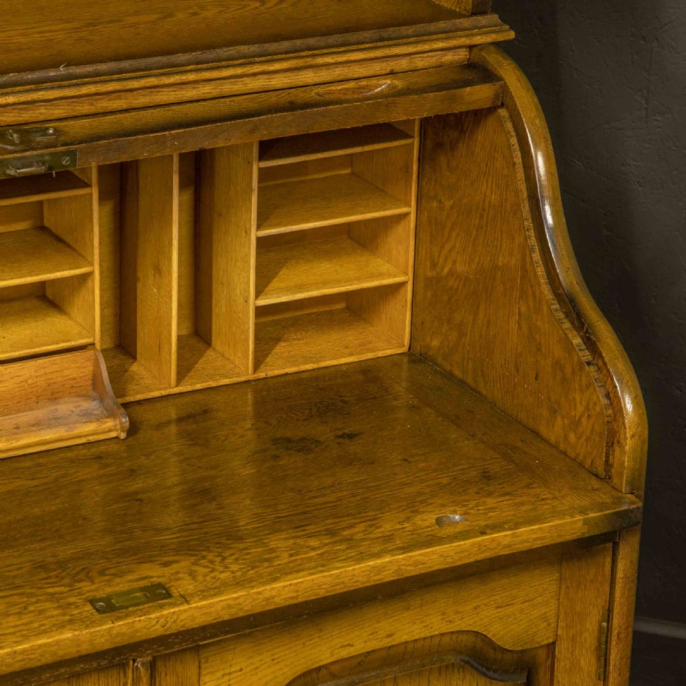 An Edwardian oak roll top bureau bookcase featuring an upper cabinet with two leaded glass doors, a central curved tambour writing section, and a two-door lower cupboard. View VIII