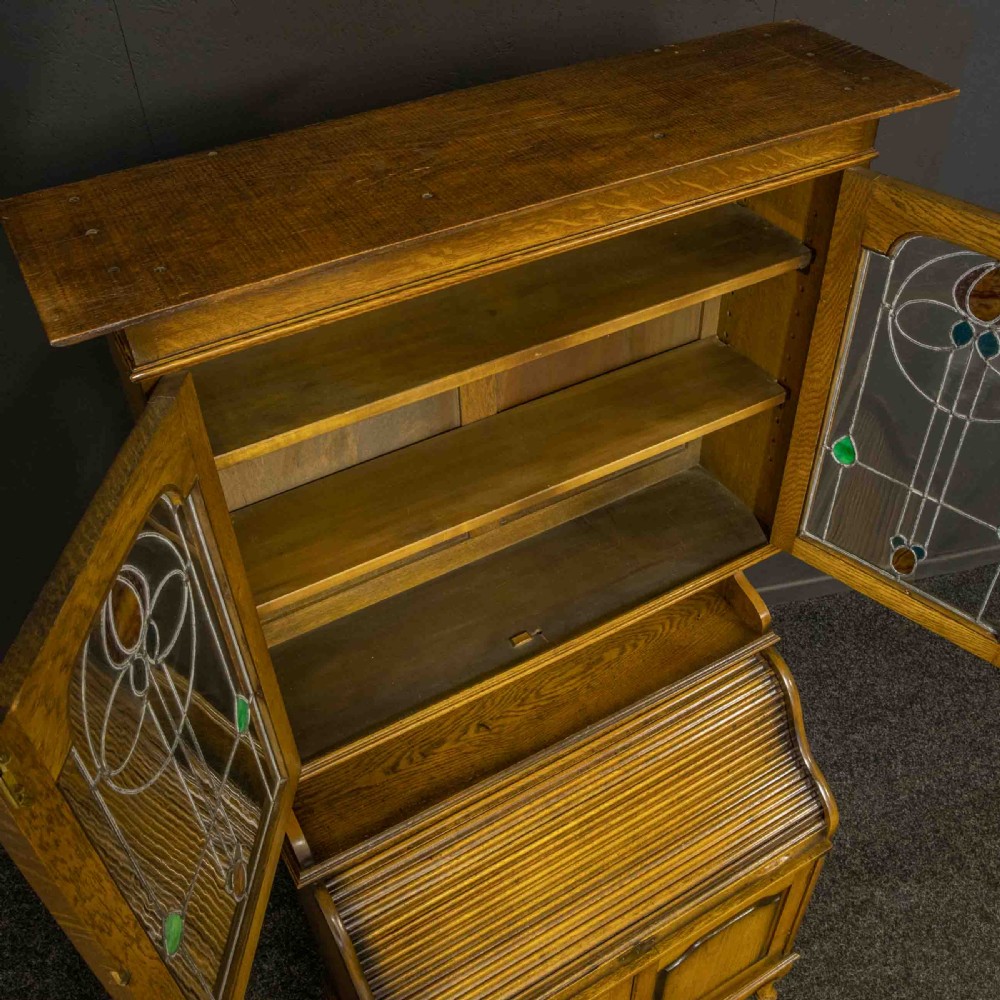 An Edwardian oak roll top bureau bookcase featuring an upper cabinet with two leaded glass doors, a central curved tambour writing section, and a two-door lower cupboard. View IX