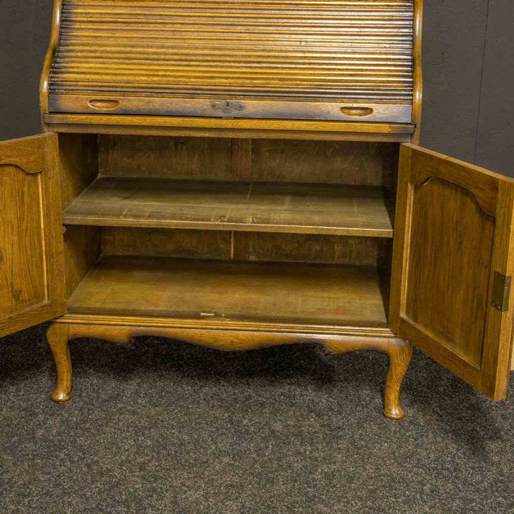 An Edwardian oak roll top bureau bookcase featuring an upper cabinet with two leaded glass doors, a central curved tambour writing section, and a two-door lower cupboard. View X