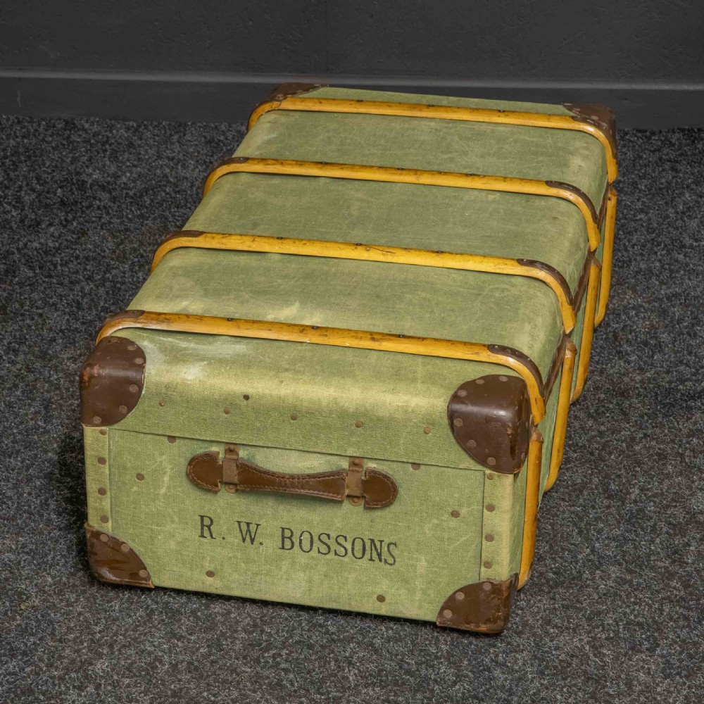 An olive green canvas-covered steamer trunk featuring wooden bentwood slats, leather corner protectors, leather side handles, and stencilled black lettering.