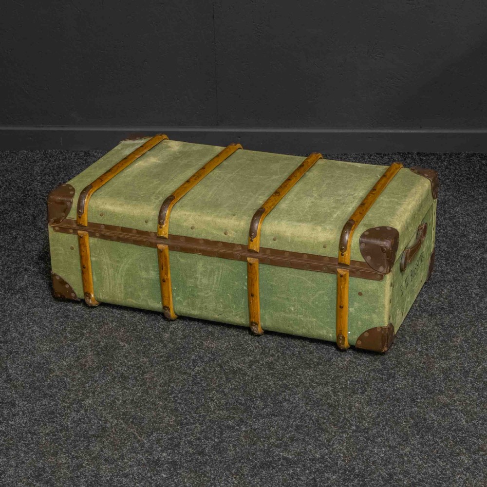 An olive green canvas-covered steamer trunk featuring wooden bentwood slats, leather corner protectors, leather side handles, and stencilled black lettering. View IV