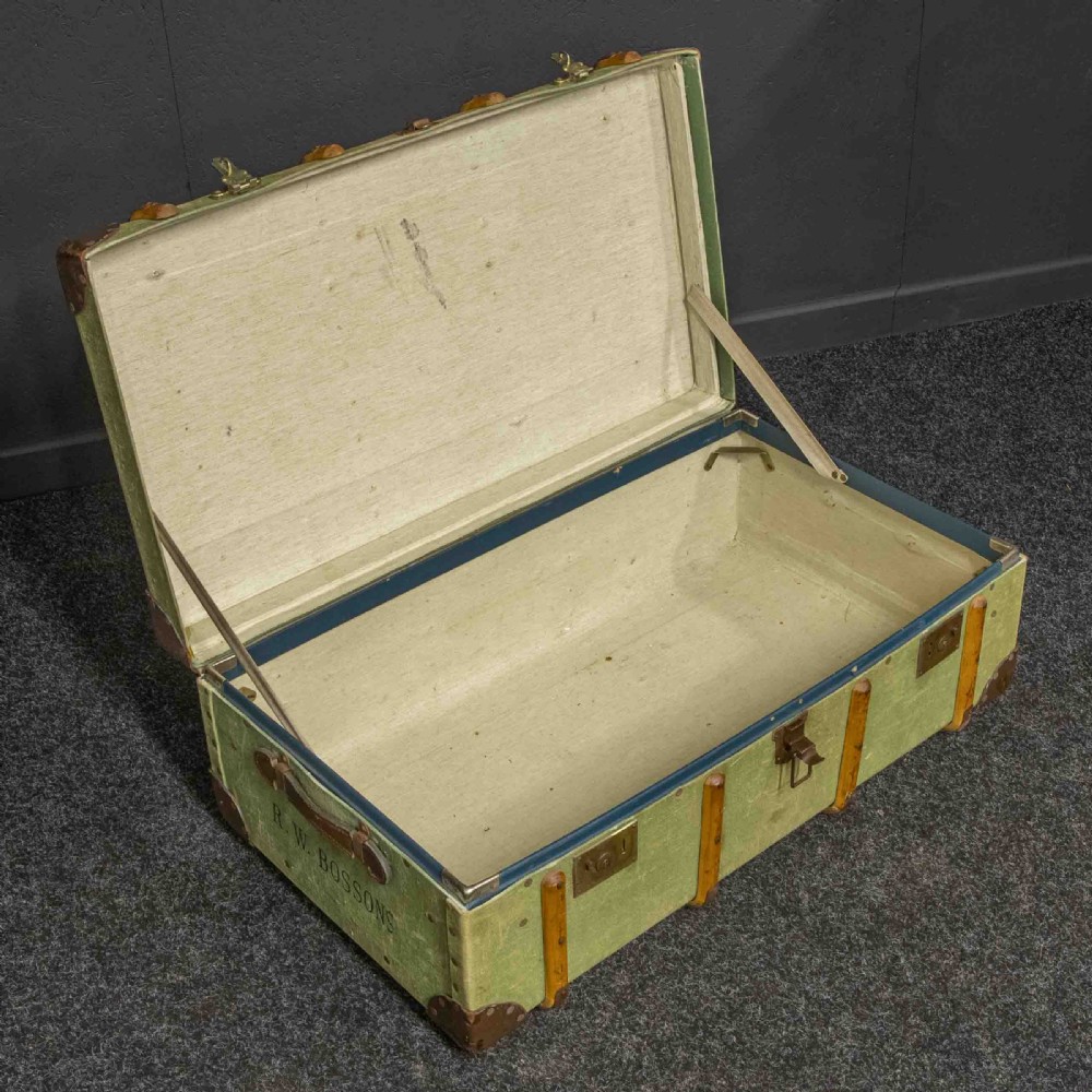 An olive green canvas-covered steamer trunk featuring wooden bentwood slats, leather corner protectors, leather side handles, and stencilled black lettering. View VI