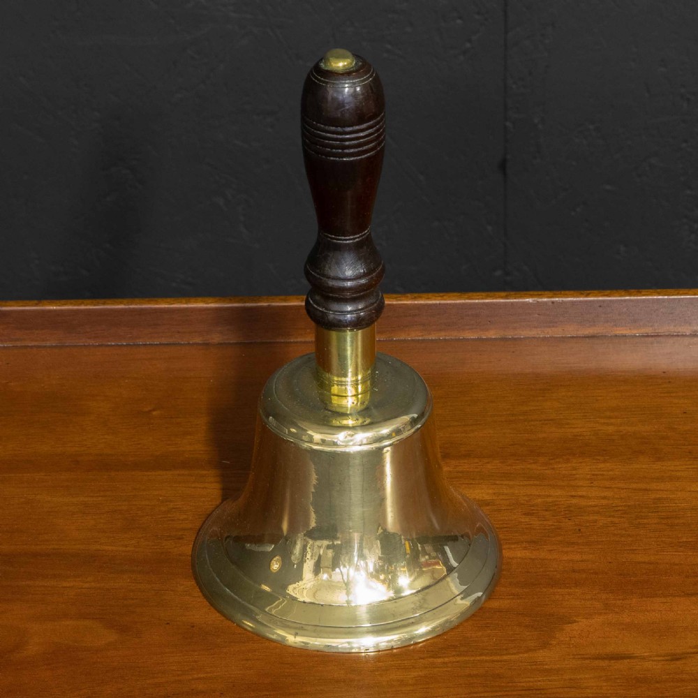 A Victorian brass handbell featuring a polished flare-mouthed bell and a dark turned wood handle with ribbed detailing.