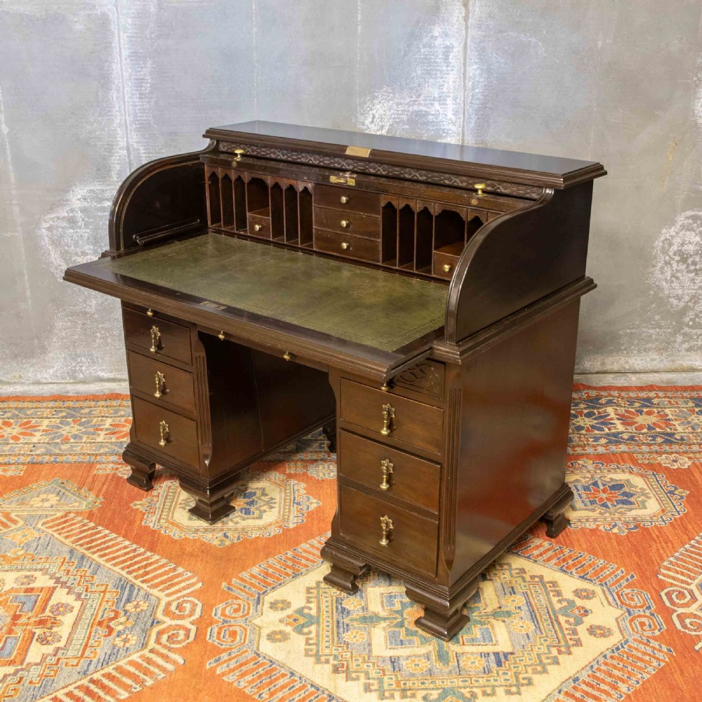 An early 20th-century Chippendale style dark mahogany roll-top desk featuring a green leather writing surface, fitted interior pigeonholes, twin drawer pedestals, and brass drop handles.