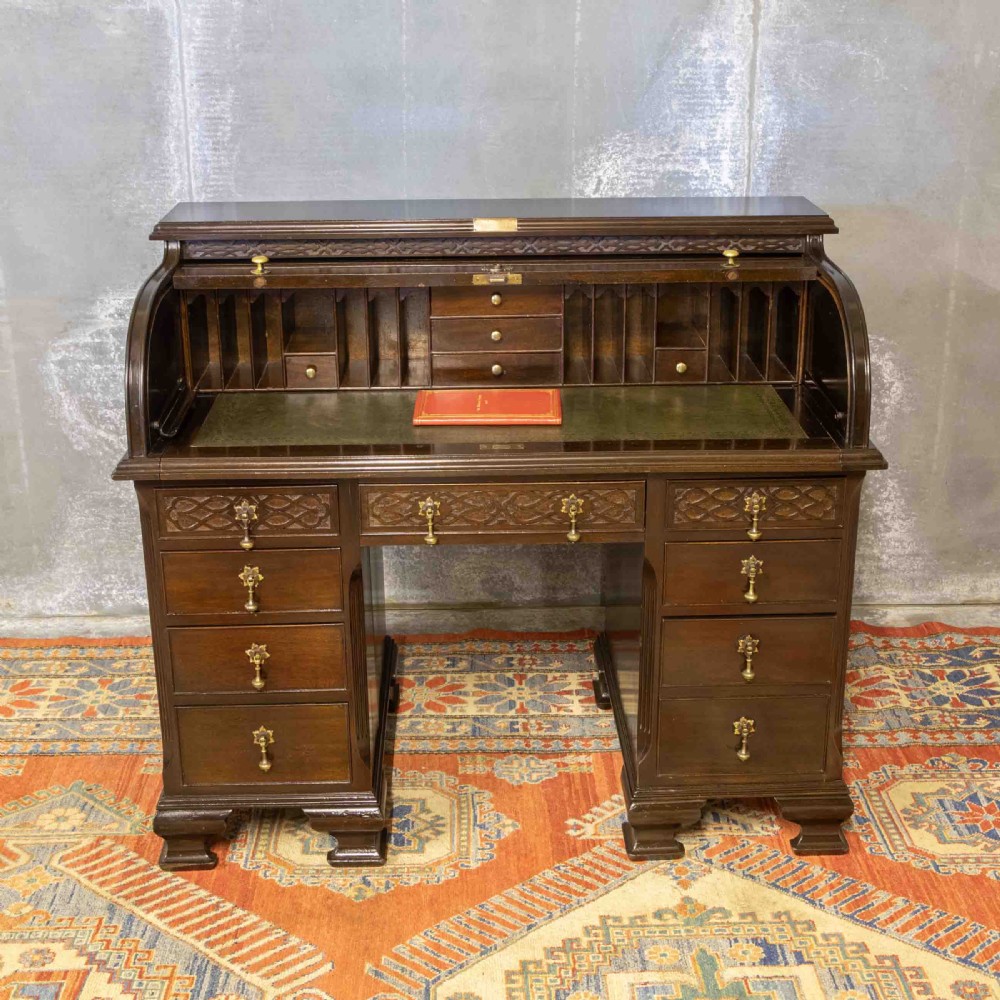 An early 20th-century Chippendale style dark mahogany roll-top desk featuring a green leather writing surface, fitted interior pigeonholes, twin drawer pedestals, and brass drop handles. View II