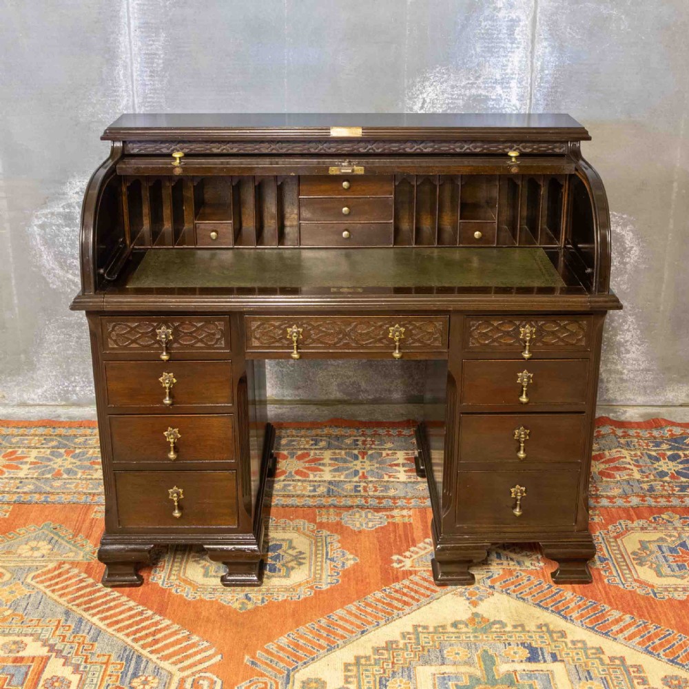 An early 20th-century Chippendale style dark mahogany roll-top desk featuring a green leather writing surface, fitted interior pigeonholes, twin drawer pedestals, and brass drop handles. View III