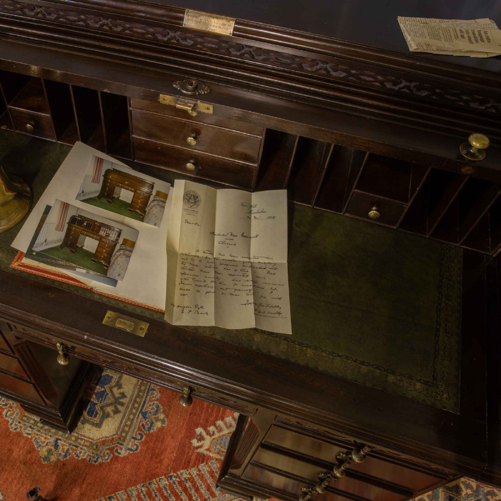 An early 20th-century Chippendale style dark mahogany roll-top desk featuring a green leather writing surface, fitted interior pigeonholes, twin drawer pedestals, and brass drop handles. View VI