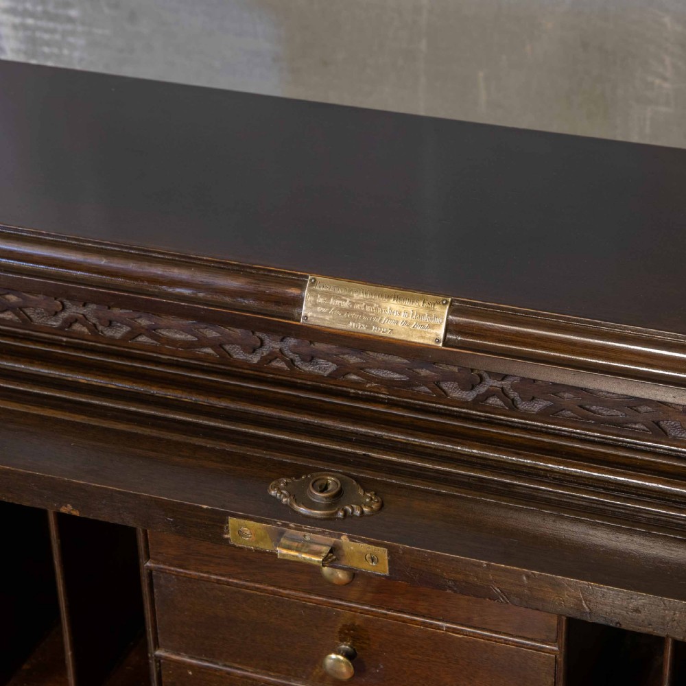 An early 20th-century Chippendale style dark mahogany roll-top desk featuring a green leather writing surface, fitted interior pigeonholes, twin drawer pedestals, and brass drop handles. View VIII