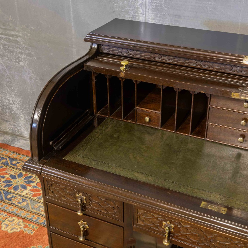 An early 20th-century Chippendale style dark mahogany roll-top desk featuring a green leather writing surface, fitted interior pigeonholes, twin drawer pedestals, and brass drop handles. View IX