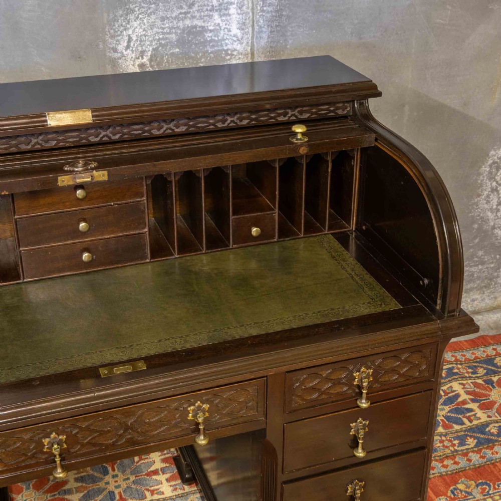 An early 20th-century Chippendale style dark mahogany roll-top desk featuring a green leather writing surface, fitted interior pigeonholes, twin drawer pedestals, and brass drop handles. View X
