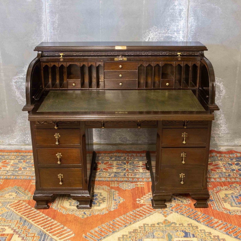 An early 20th-century Chippendale style dark mahogany roll-top desk featuring a green leather writing surface, fitted interior pigeonholes, twin drawer pedestals, and brass drop handles. View XV