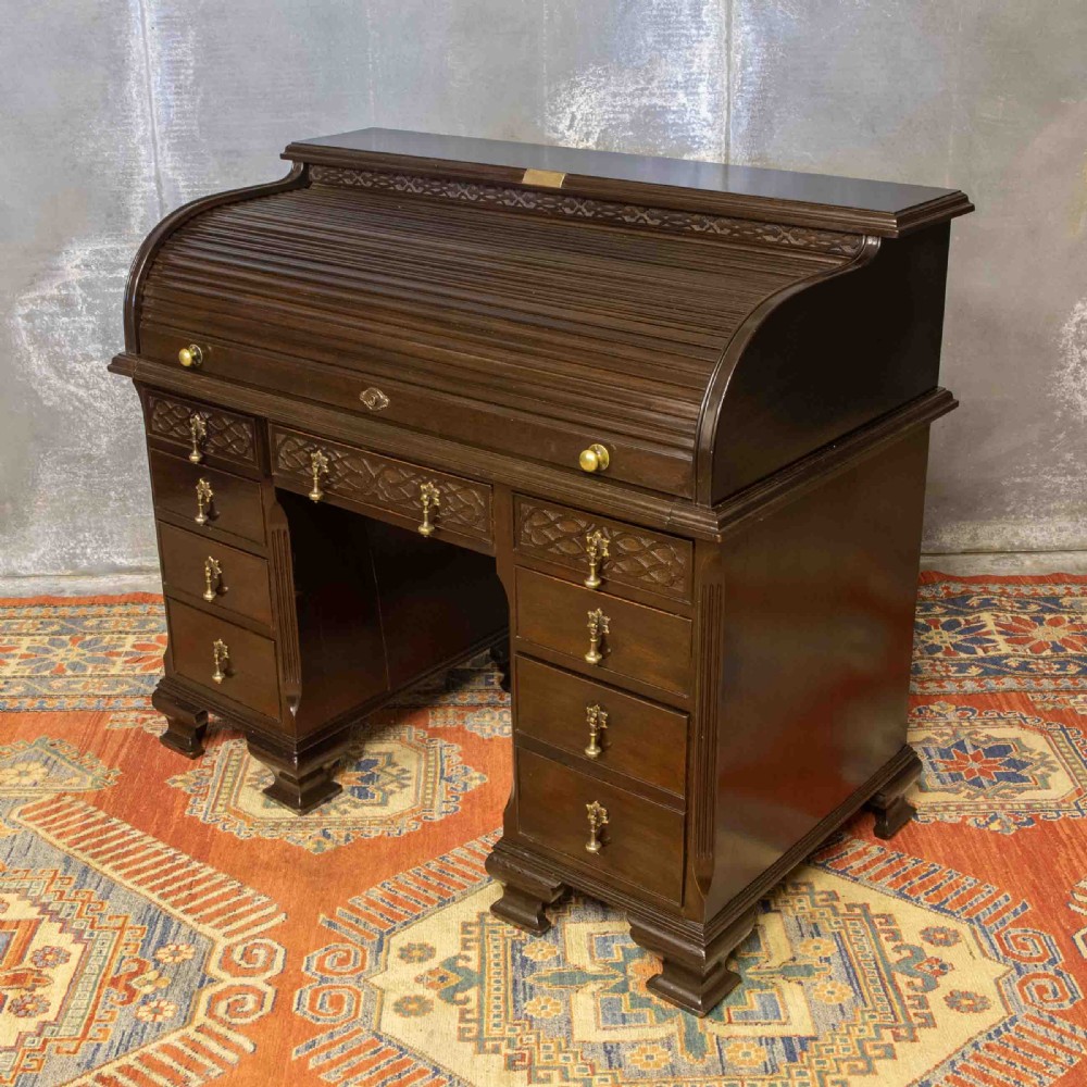 An early 20th-century Chippendale style dark mahogany roll-top desk featuring a green leather writing surface, fitted interior pigeonholes, twin drawer pedestals, and brass drop handles. View XVI