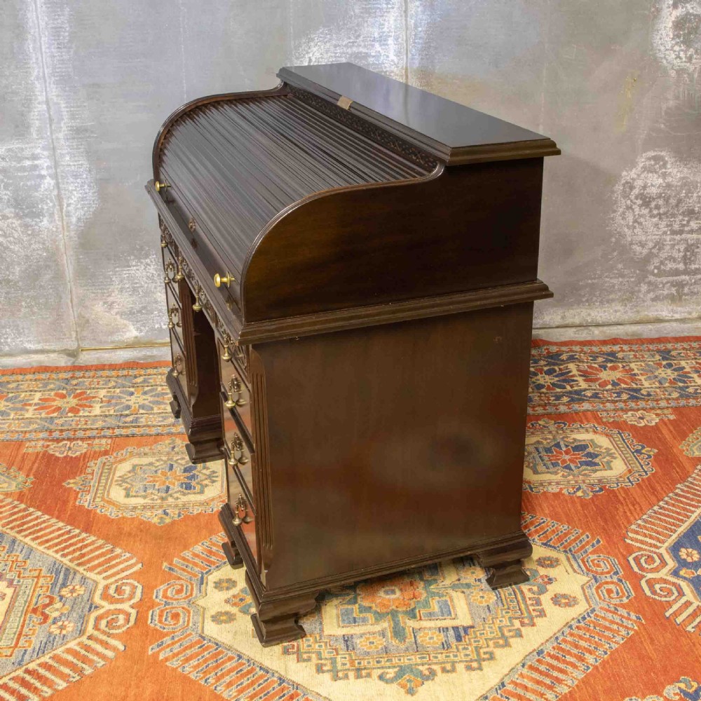 An early 20th-century Chippendale style dark mahogany roll-top desk featuring a green leather writing surface, fitted interior pigeonholes, twin drawer pedestals, and brass drop handles. View XVII