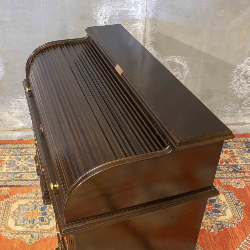 An early 20th-century Chippendale style dark mahogany roll-top desk featuring a green leather writing surface, fitted interior pigeonholes, twin drawer pedestals, and brass drop handles. View XIX