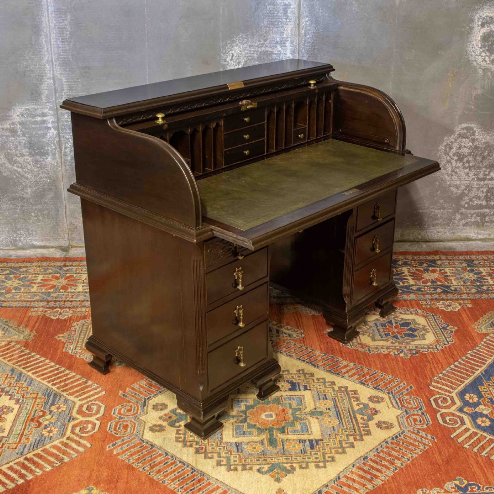 An early 20th-century Chippendale style dark mahogany roll-top desk featuring a green leather writing surface, fitted interior pigeonholes, twin drawer pedestals, and brass drop handles. View XXII