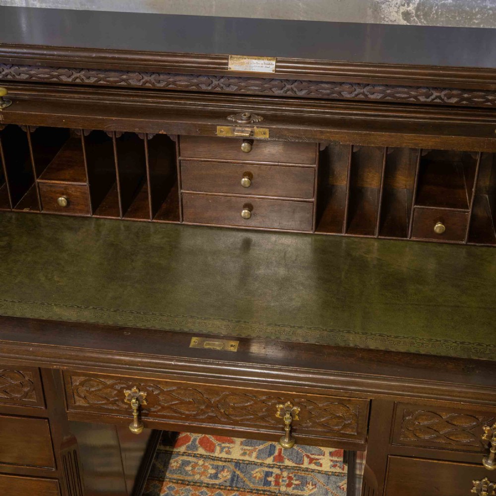 An early 20th-century Chippendale style dark mahogany roll-top desk featuring a green leather writing surface, fitted interior pigeonholes, twin drawer pedestals, and brass drop handles. View XXIII