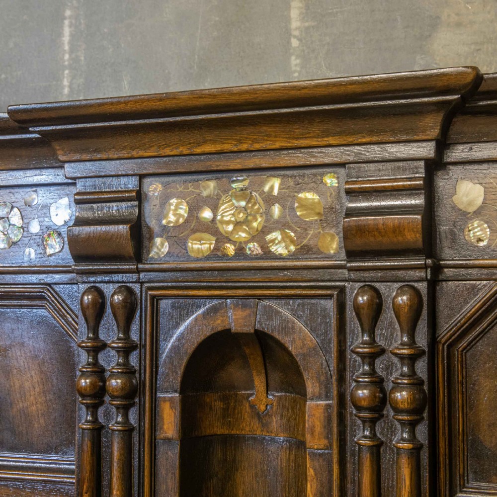 A dark oak Jacobean dresser featuring geometric mouldings, mother-of-pearl inlays, arched panels, turned split spindles, and lower drawers. View X