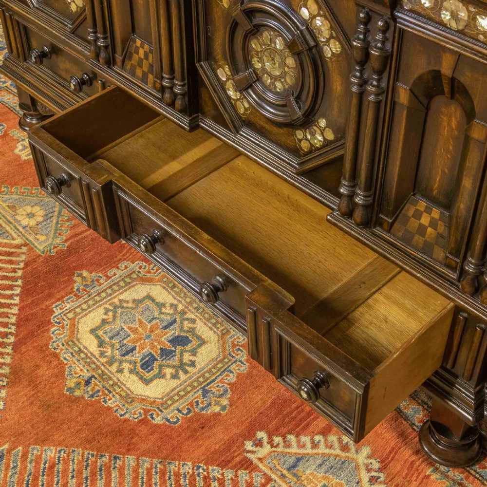 A dark oak Jacobean dresser featuring geometric mouldings, mother-of-pearl inlays, arched panels, turned split spindles, and lower drawers. View XI