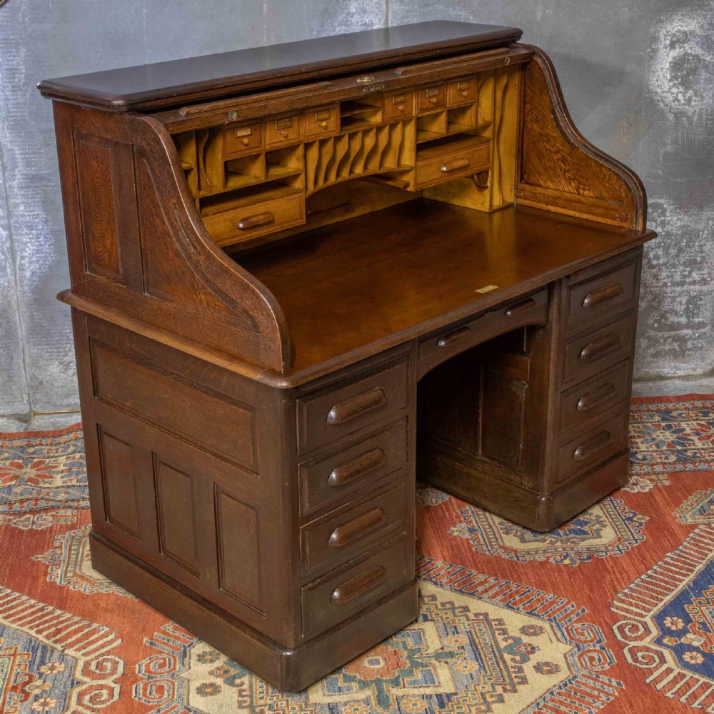 A late Victorian oak roll-top desk with an open tambour shutter revealing internal pigeonholes above a twin-pedestal base with wooden handles.