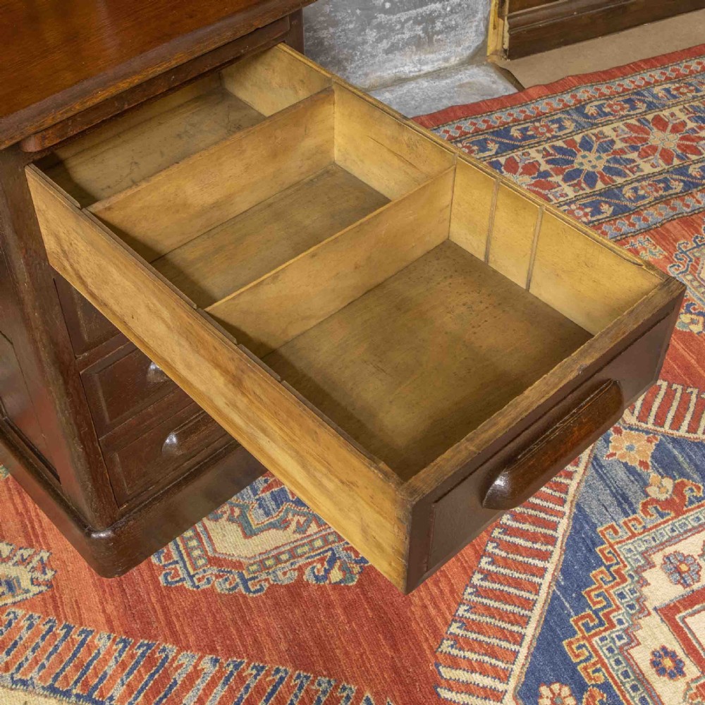 A late Victorian oak roll-top desk with an open tambour shutter revealing internal pigeonholes above a twin-pedestal base with wooden handles. View II