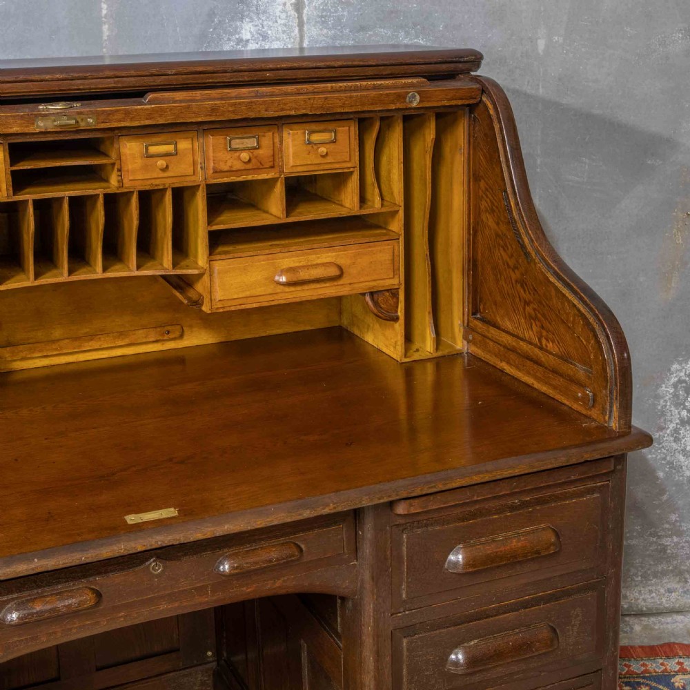 A late Victorian oak roll-top desk with an open tambour shutter revealing internal pigeonholes above a twin-pedestal base with wooden handles. View III