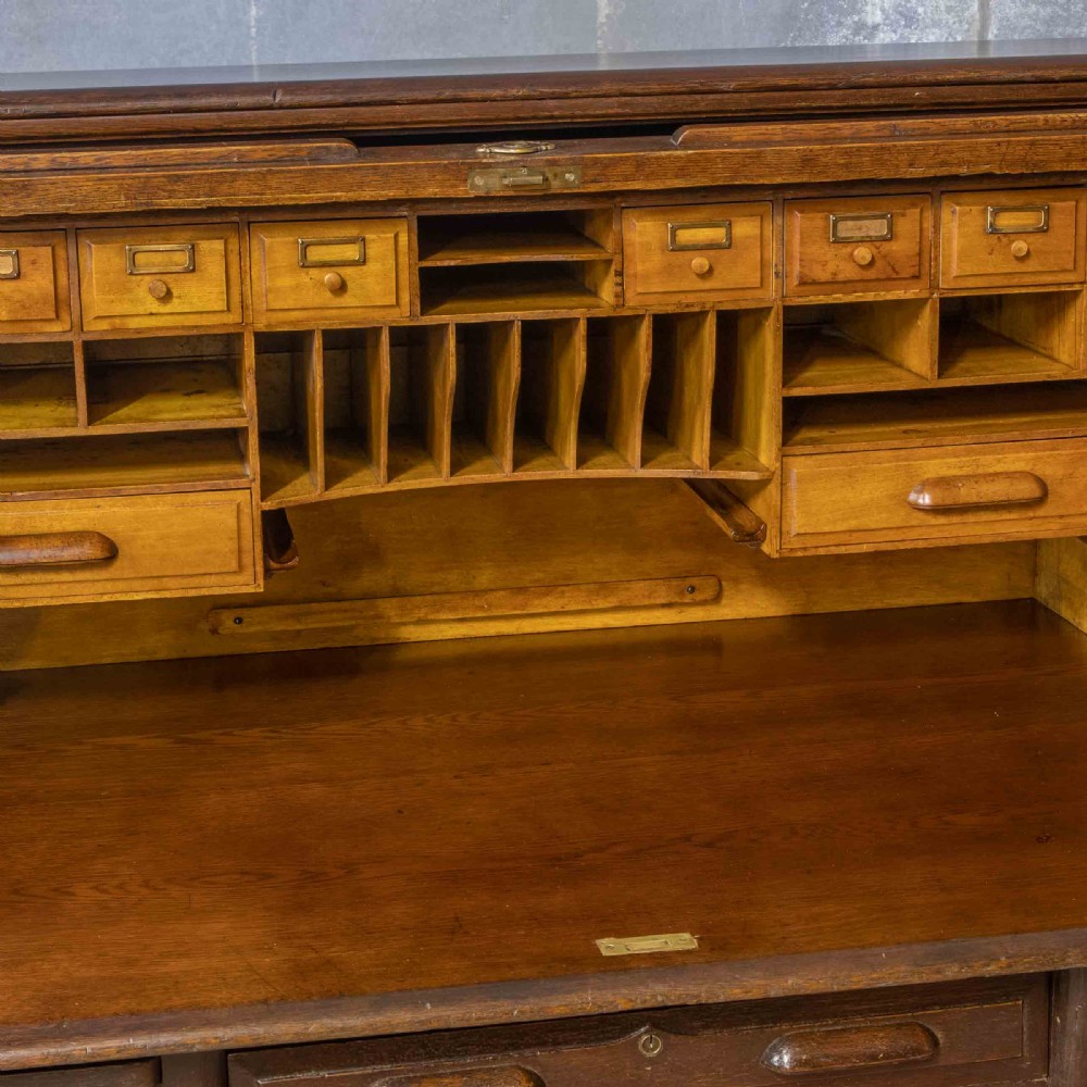 A late Victorian oak roll-top desk with an open tambour shutter revealing internal pigeonholes above a twin-pedestal base with wooden handles. View V