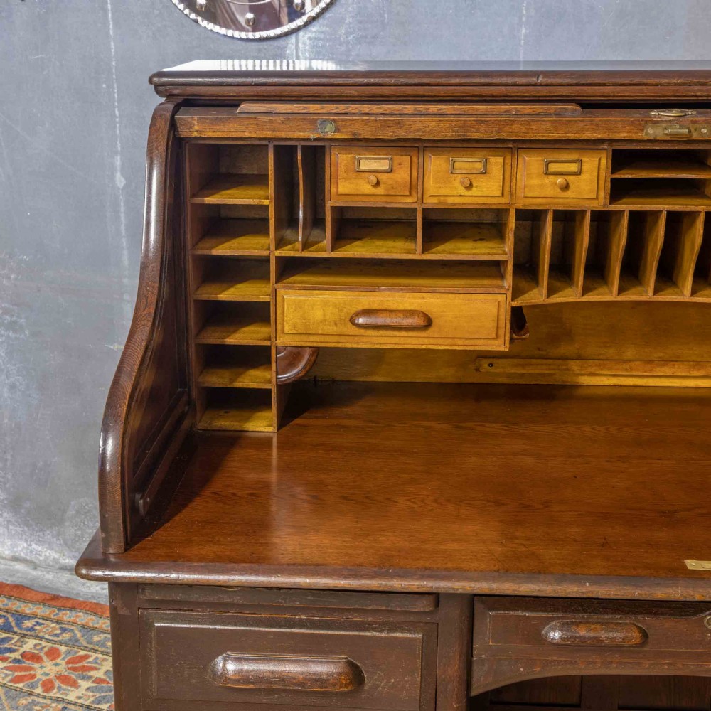 A late Victorian oak roll-top desk with an open tambour shutter revealing internal pigeonholes above a twin-pedestal base with wooden handles. View VI