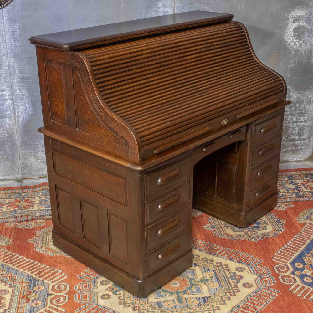 A late Victorian oak roll-top desk with an open tambour shutter revealing internal pigeonholes above a twin-pedestal base with wooden handles. View VII