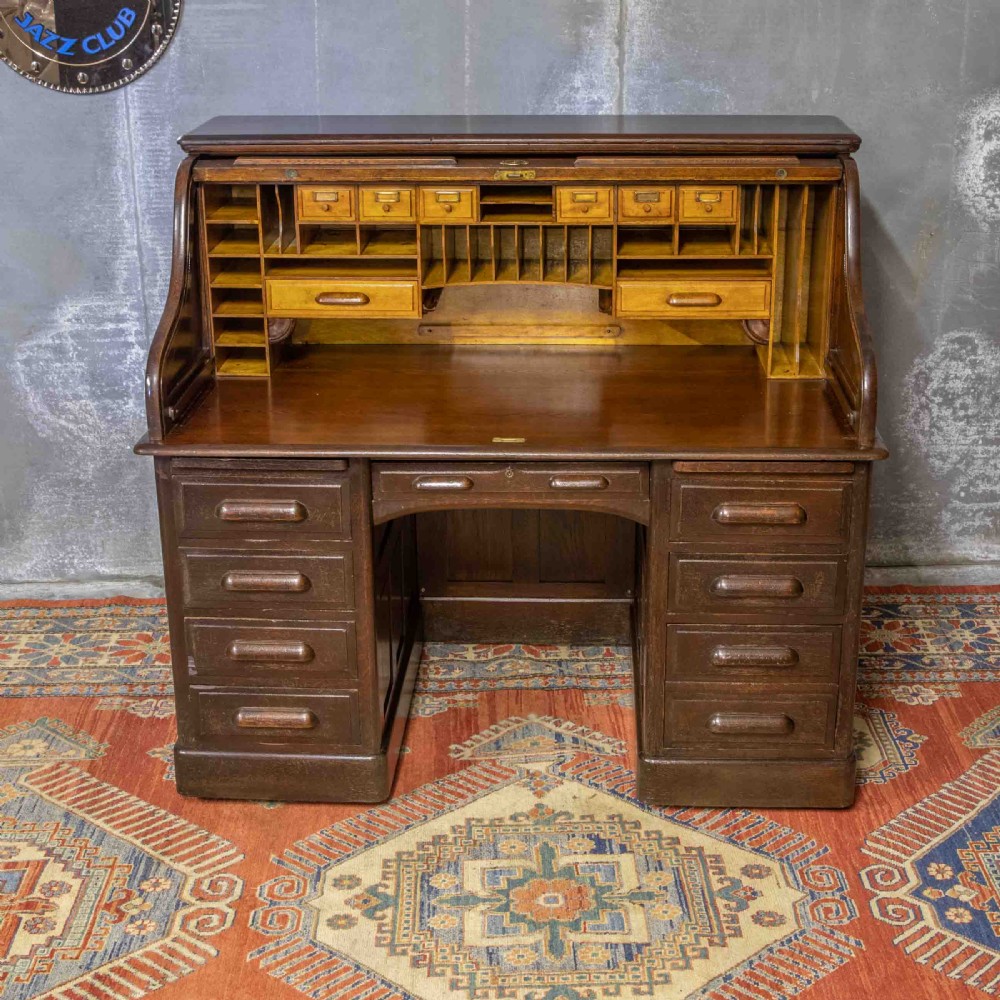 A late Victorian oak roll-top desk with an open tambour shutter revealing internal pigeonholes above a twin-pedestal base with wooden handles. View X