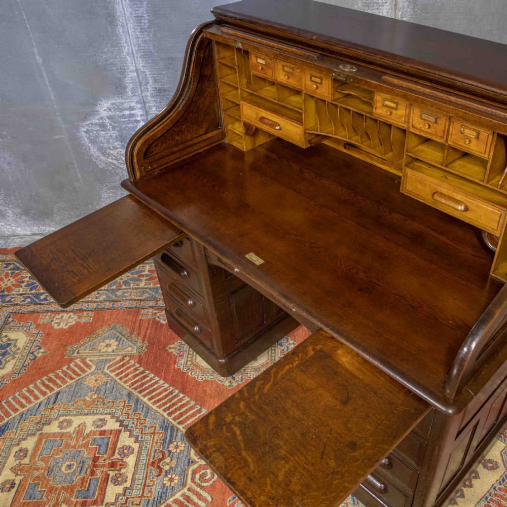 A late Victorian oak roll-top desk with an open tambour shutter revealing internal pigeonholes above a twin-pedestal base with wooden handles. View XII