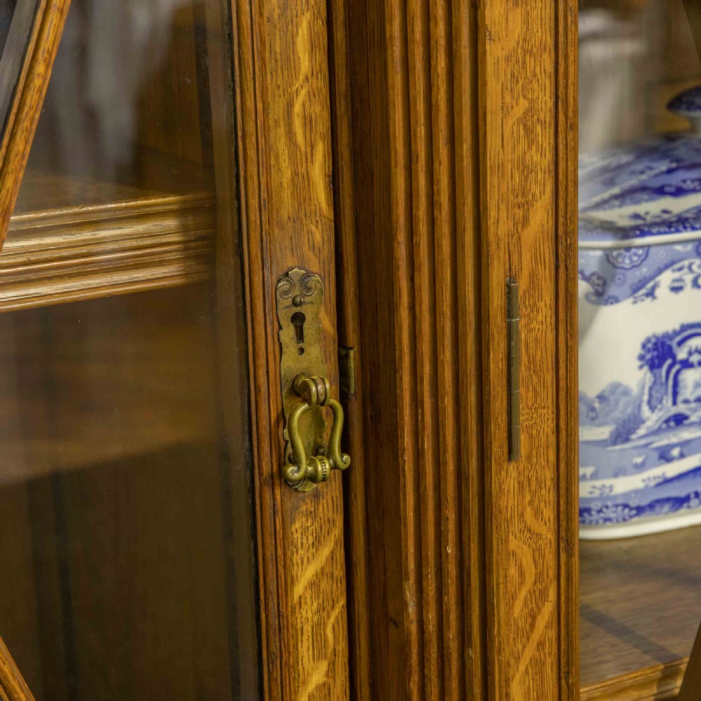 An Edwardian oak breakfront bookcase featuring four glazed upper doors with geometric astragal bars, carved lower panel doors, and a decorative carved top pediment. View IV