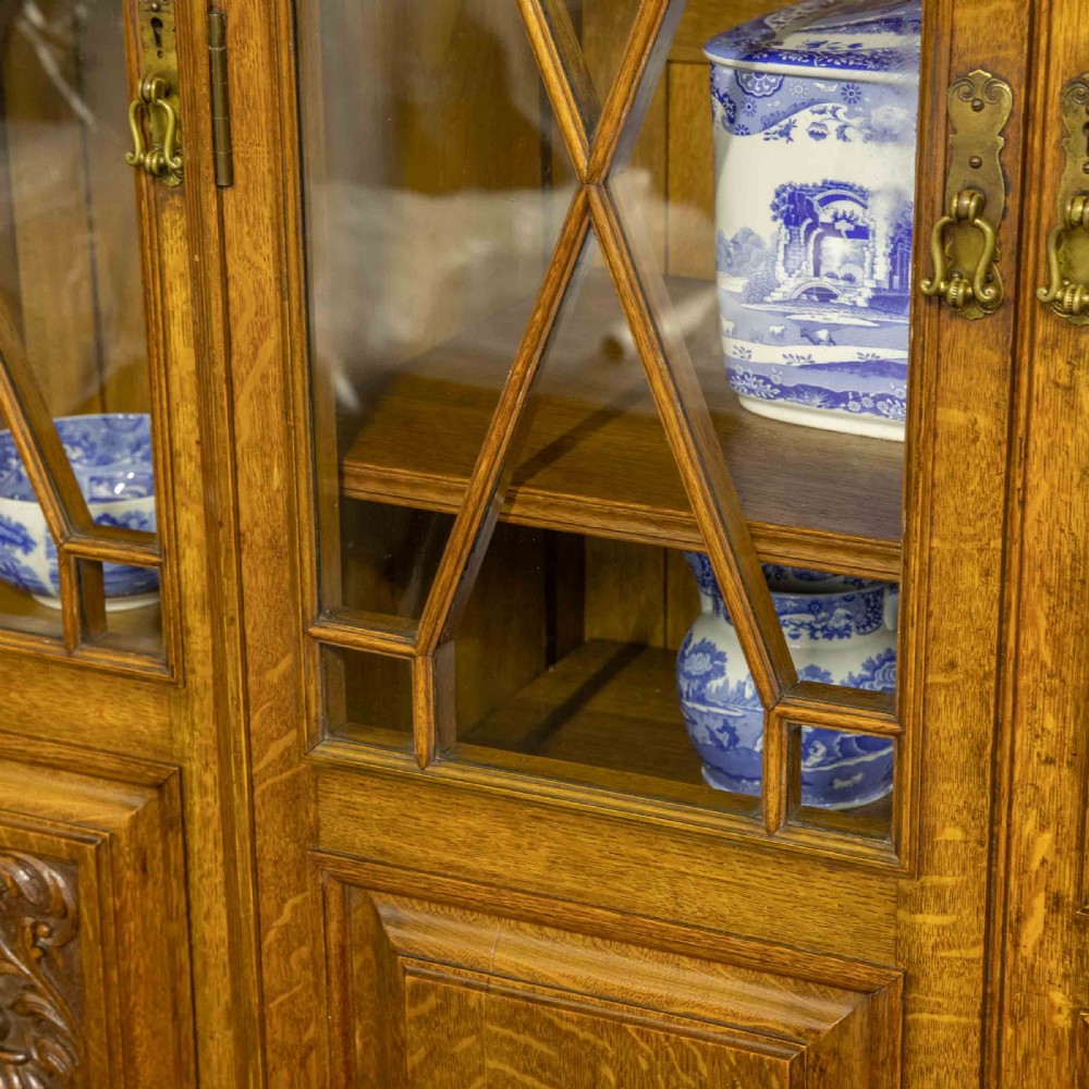 An Edwardian oak breakfront bookcase featuring four glazed upper doors with geometric astragal bars, carved lower panel doors, and a decorative carved top pediment. View V