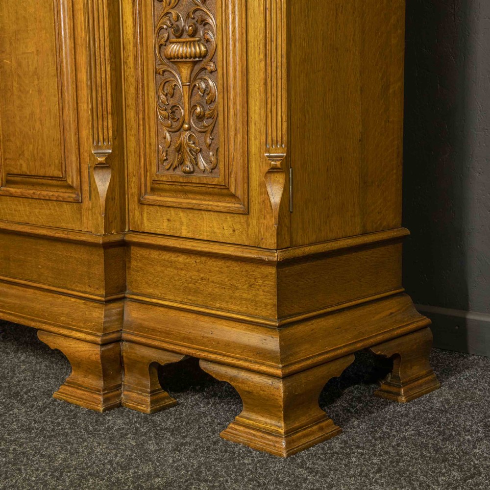 An Edwardian oak breakfront bookcase featuring four glazed upper doors with geometric astragal bars, carved lower panel doors, and a decorative carved top pediment. View XIV