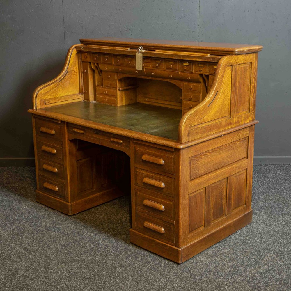 An Edwardian oak roll top desk with a raised slatted tambour front revealing fitted interior compartments above twin pedestal drawers.
