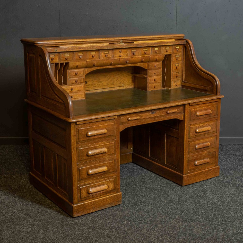 An Edwardian oak roll top desk with a raised slatted tambour front revealing fitted interior compartments above twin pedestal drawers. View II